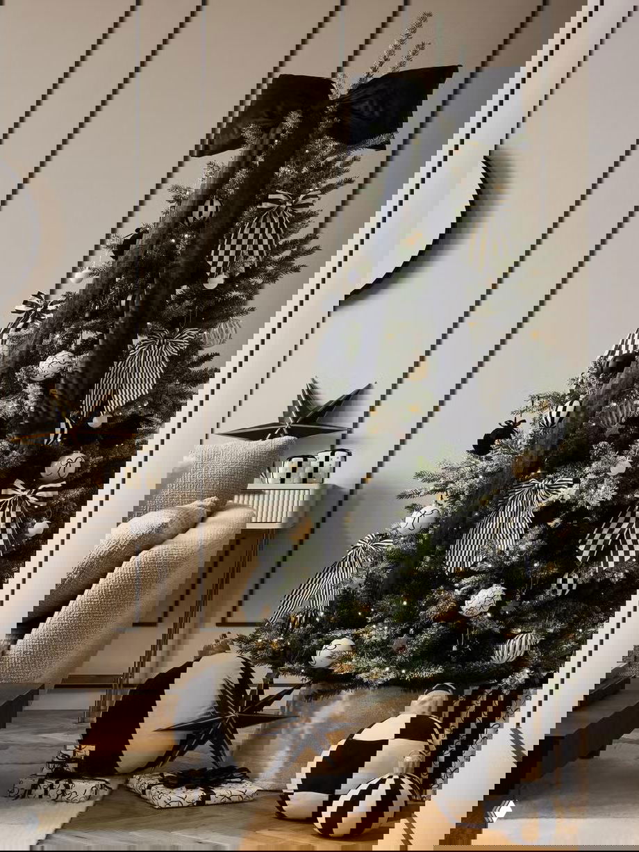 Черно‑белая праздничная елка с большими полосатыми бантами и декоративными шарами; интерьер в нейтральных тонах с акцентом на графичные орнаменты.