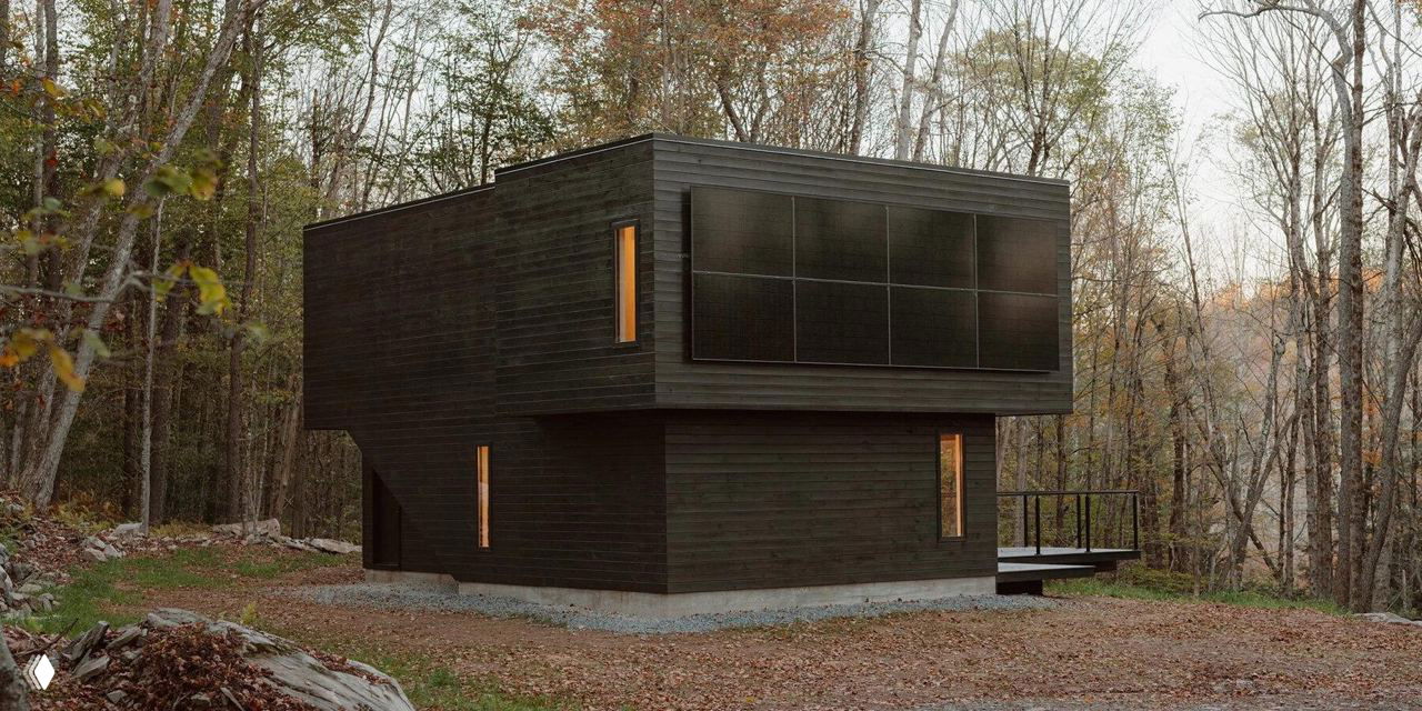 Экстерьер Forest Edge House: тёмный деревянный двухэтажный дом на лесном склоне в Катскиллс, видны монокристаллические панели, узкие вертикальные окна и лесной контекст вокруг.