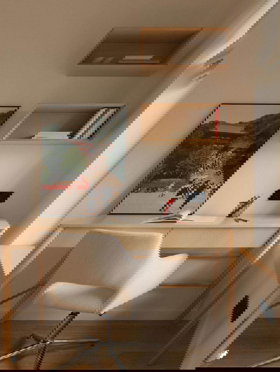 Домашний рабочий стол у окна: светлый деревянный стол, мягкое кресло и настенный плакат с японской сценой, сочетание винтажных акцентов и минимализма.