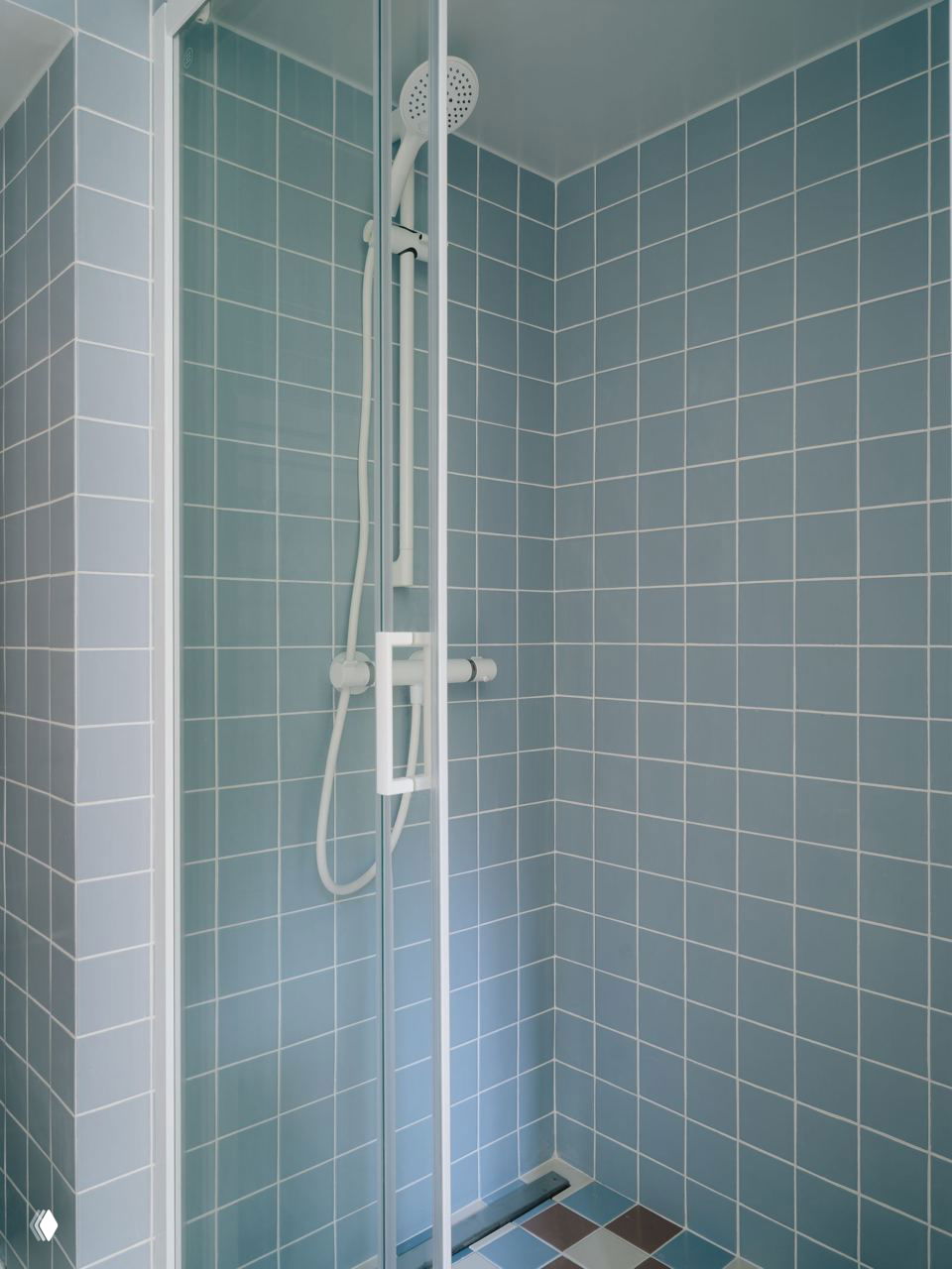 Детали ванной комнаты: голубая плитка на стенах и полу, белая округлая раковина и встроенные шкафчики из светлой фанеры в морской цветовой гамме проекта.