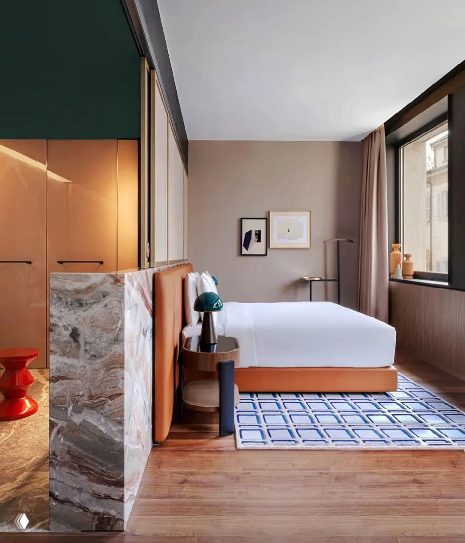 Номер отеля с большой кроватью, стеклянными перегородками в ванной и мраморной отделкой на полу и перегородке возле спальни.