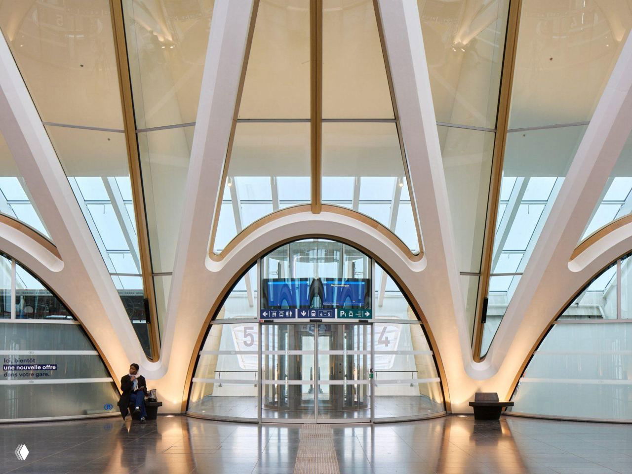 Интерьер станции: белые арочные опоры и стеклянные перепады, сквозные входы и минималистичные электронные табло над дверями.