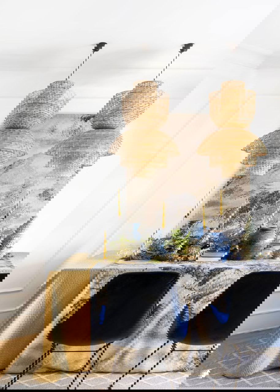 Столовая зона с плетеными подвесными светильниками, столом, украшенным растениями, керамикой и золотыми свечами — сочетание натуральных материалов и праздничных акцентов.