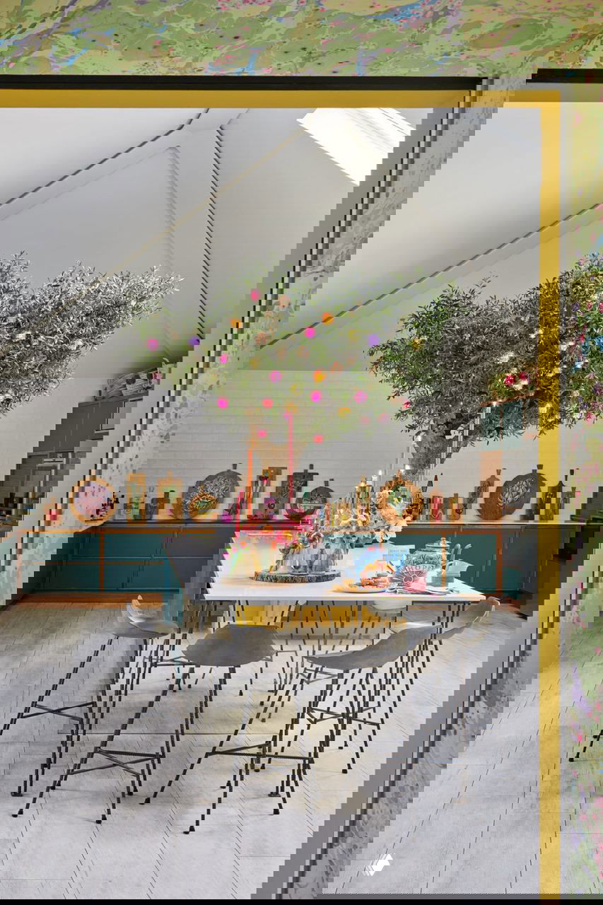 Кухня со столом и большим оливковым деревом, украшенным шарами; дерево «растет» из острова, стол сервирован свечами и яркими декорами.