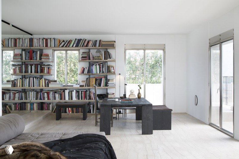 Угловая рабочая зона с настенными полками, книгами и мягкой зоной отдыха; большие окна наполняют пространство дневным светом.