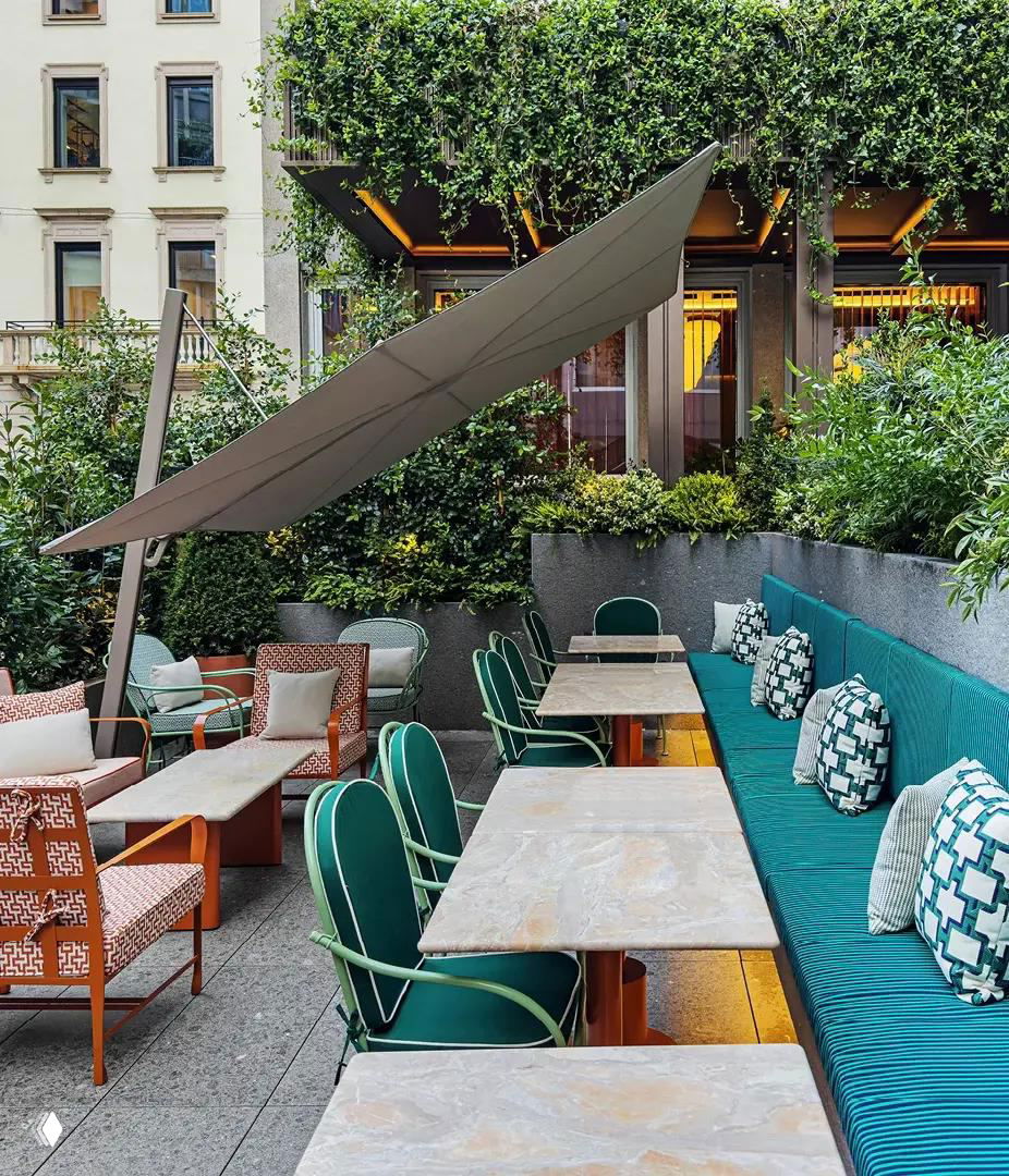 Открытая терраса отеля Casa Brera: зелёные растения, бирюзовые диваны и уютные обеденные зоны на свежем воздухе в центре Милана.