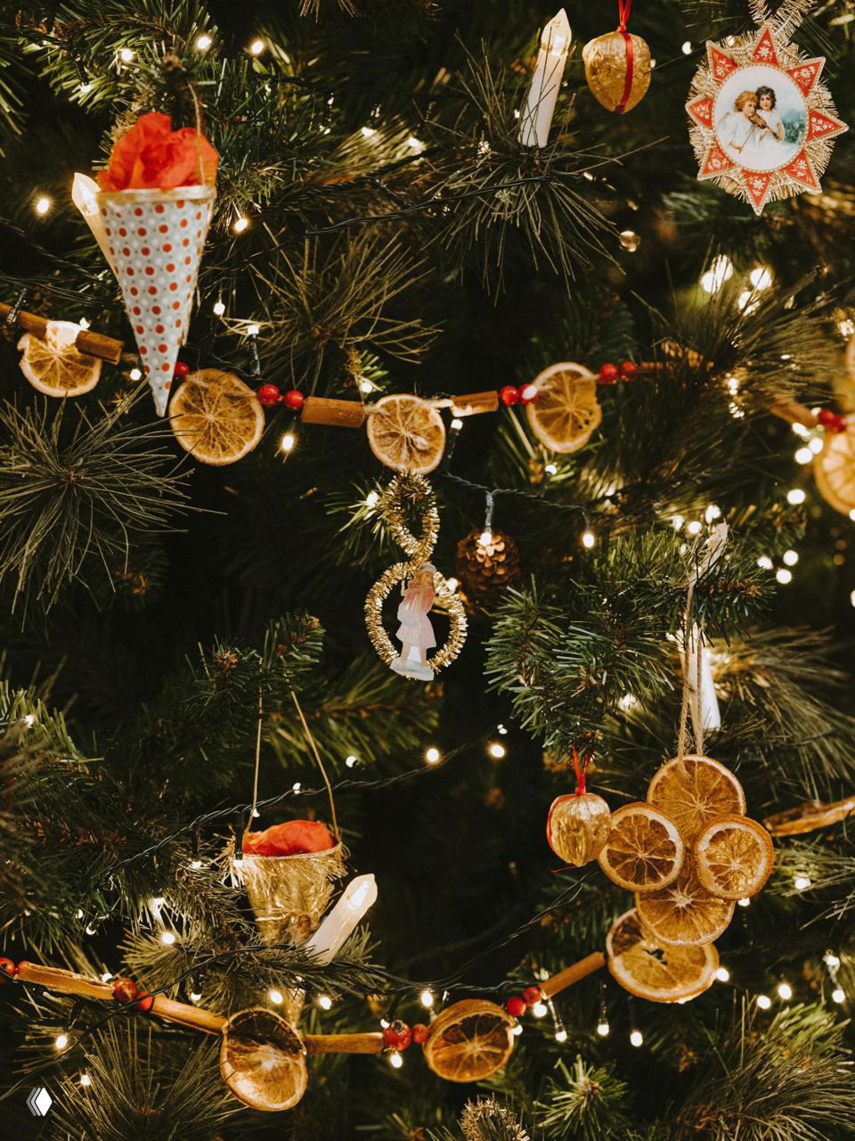 Ёлочные украшения ручной работы: гирлянда из высушенных апельсинов, корицы и огоньков на ветвях ёлки в небольшой комнате
