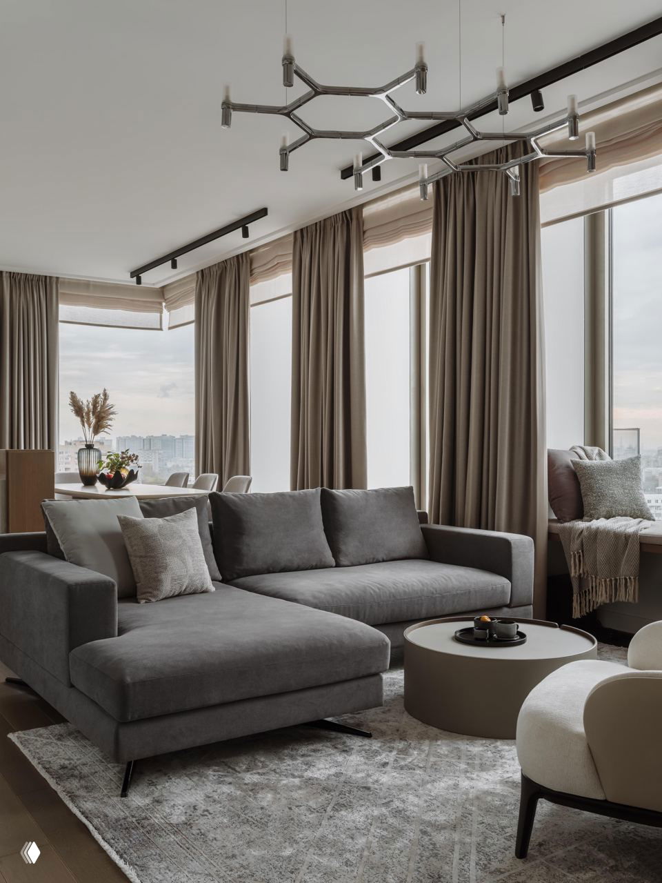 Светлая гостиная в джапанди-стиле: большой серый угловой диван, круглый кофейный стол и панорамные окна с видом на Москва‑Сити, нейтральная палитра.