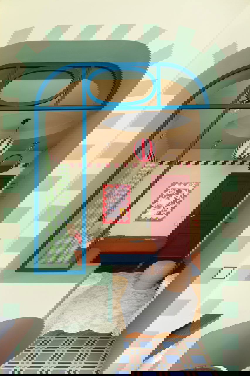 Вид через арочный проём в детскую: яркая зелёно‑бирюзовая рама окна, шарообразный светильник, ковёр и две кровати в тёплых тонах, атмосфера сказки.