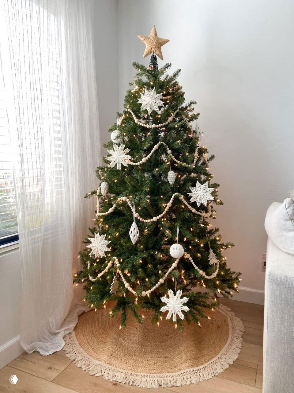 Полная композиция украшенной ёлки на круглой джутовой юбке: светлое окно, деревянный пол и натуральные текстуры в интерьере.