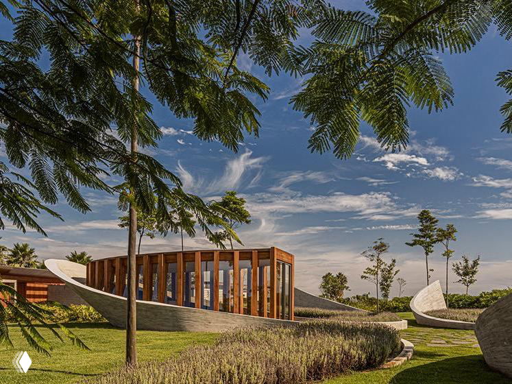 Дневной вид на капеллу в зелёном ландшафте: сочетание дерева и бетона на фоне неба, подчеркивающие простоту и уединённость объекта.