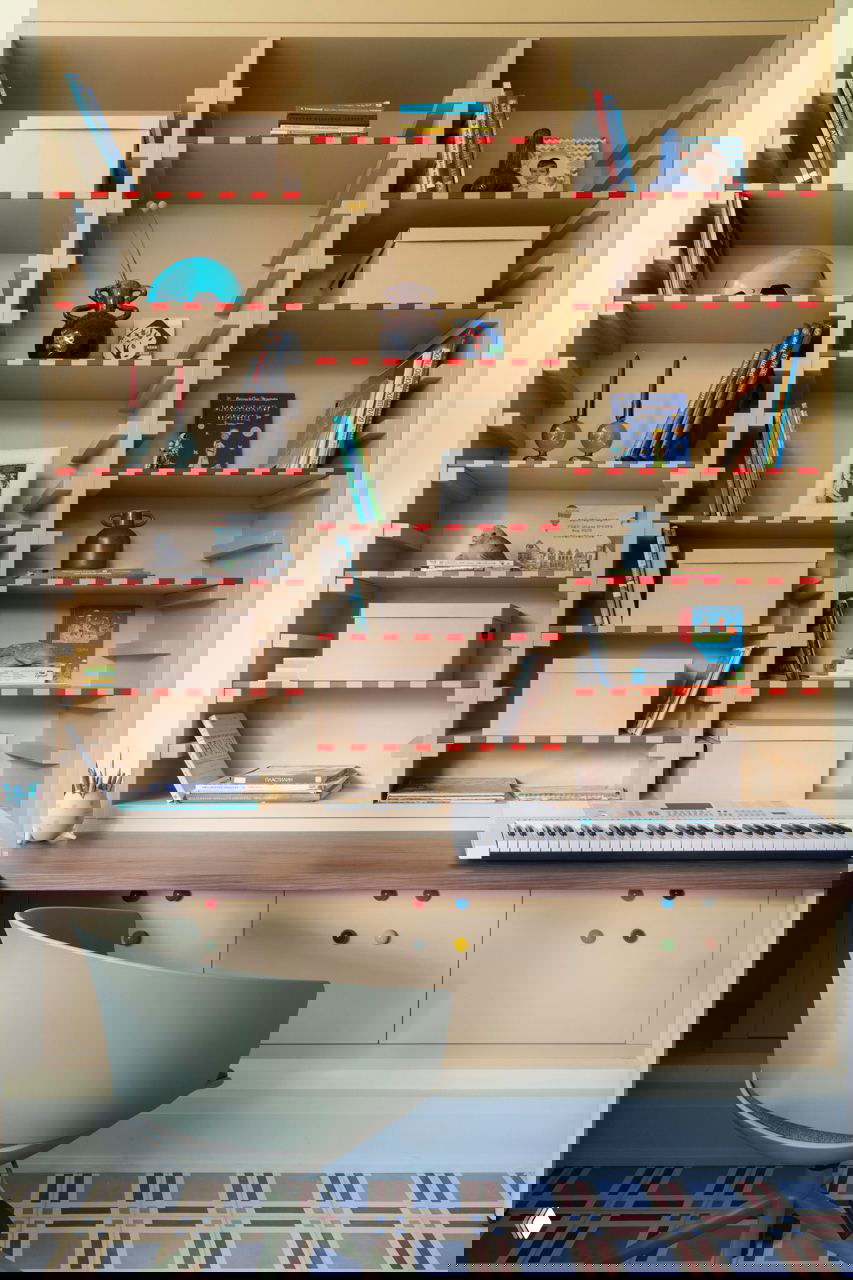 Большая встроенная стеллажная система с множеством полок и коробок, на столе синтезатор и рабочие принадлежности — организованная зона хранения и творчества.