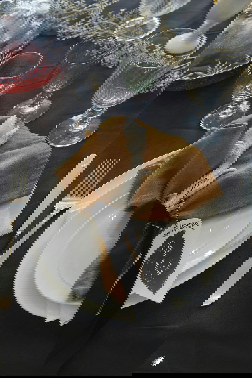 Сервировка: белая керамика, охристая льняная салфетка, декоративная керамическая роза и фирменная бирка ручной работы на тарелке.