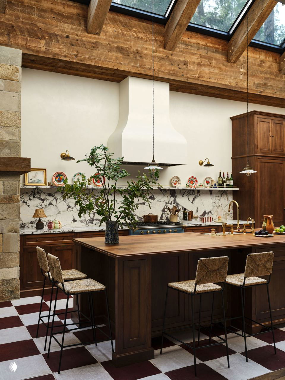 Кухня с широким деревянным островом, белой декоративной вытяжкой и мраморной стеной; сочетание натурального дерева, плитки и растительных акцентов.