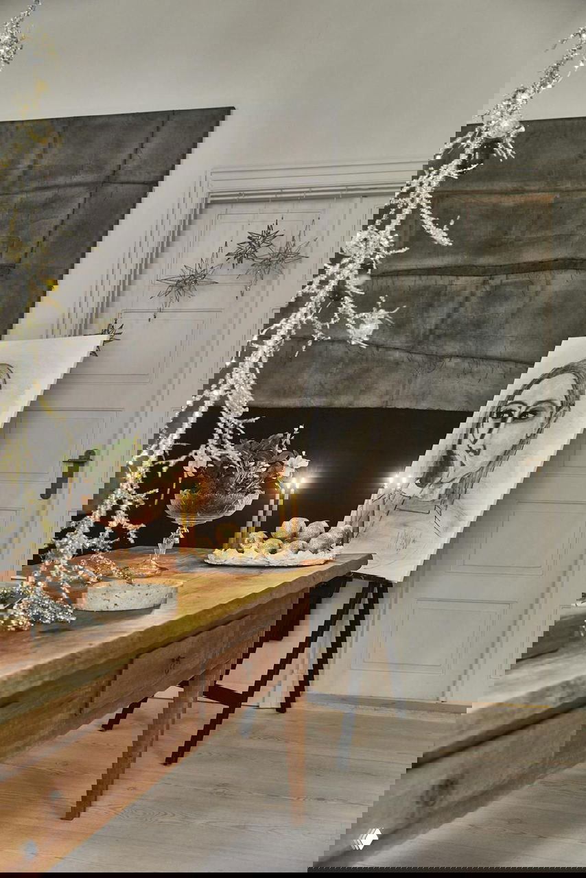 Деталь: сложенные белые тарелки, столовые приборы, набор стеклянных бокалов и украшения в виде сухих веток на темной скатерти.