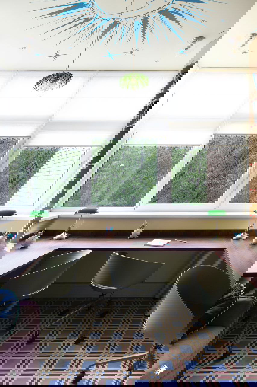 Широкая рабочая зона у большого окна с тремя стульями, зелёные лампы и декоративный узор на напольном покрытии; панорамный вид на зелёный двор.