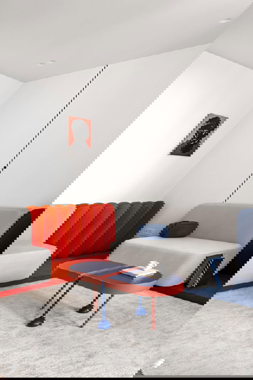 Гостиная с модульными диванами серого, красного и синего цветов, низким двучленным столиком и светлым ковром на фоне минималистичных белых стен.