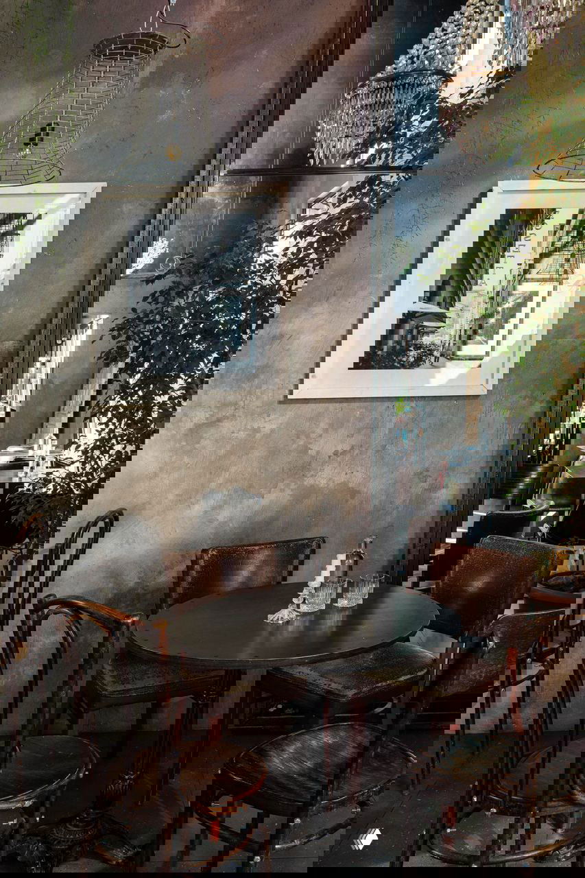 Небольшой круглый стол у стены, четыре винтажных стула, большое зеркало и зелёные растения на фоне грубой штукатурки в интерьере кафе «Ровесники», фото Кирилла Овчинникова.