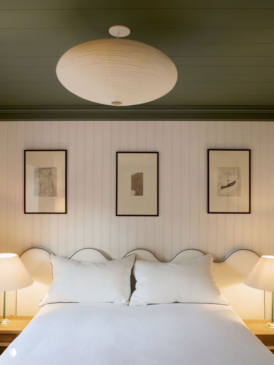 Спальная зона с большим светлым изголовьем, белым постельным бельём и тёплым ламповым светом — уютный уголок в доме у моря.