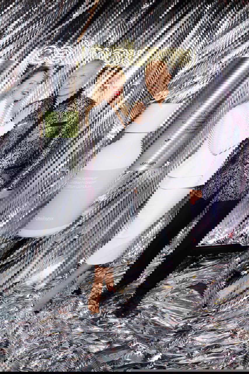 Фотозона с неоновой вывеской бренда партнёра и двое гостей позируют в вечерних образах на серебристом фоне и декоре мероприятия.