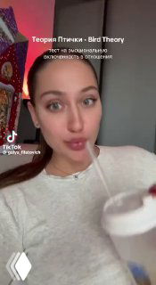 Кадр вертикального видео: молодая женщина дома с напитком в руке, нейтральное выражение лица, заметен водяной знак TikTok.