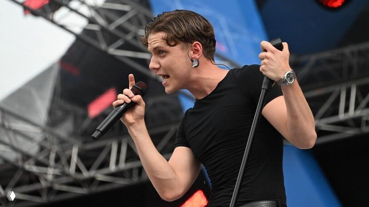 Молодой певец на сцене с микрофоном в руках, крупный план исполнителя и элементы концертной сцены на заднем плане