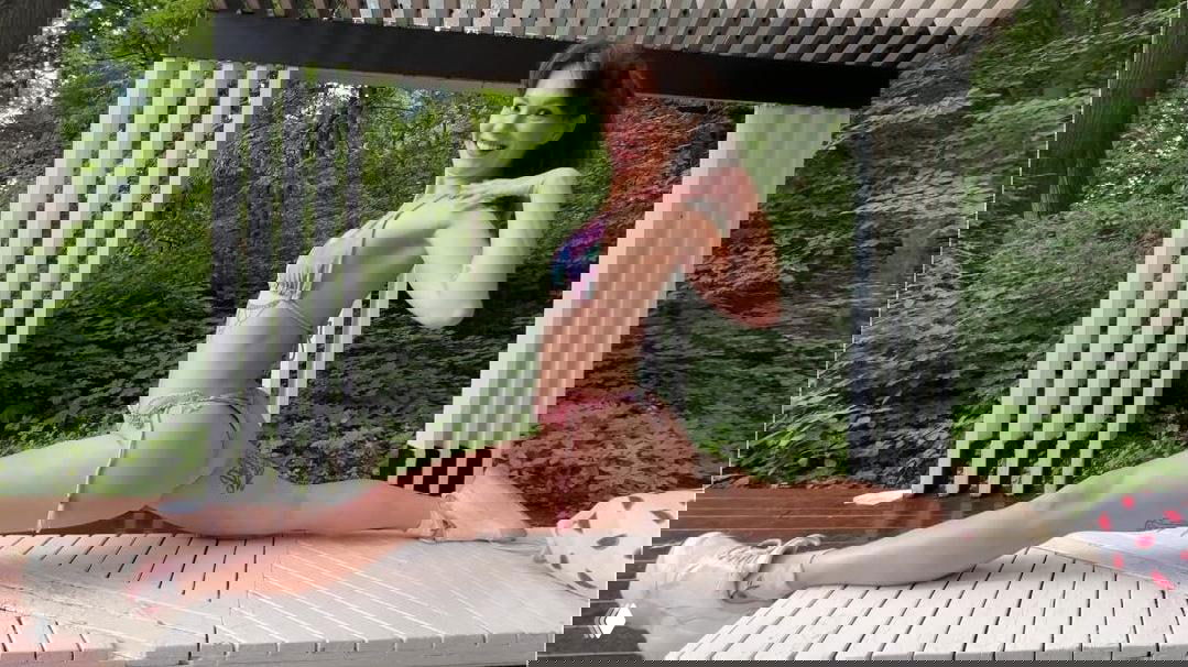 Женщина в бикини делает шпагат на деревянной платформе на фоне леса, улыбается — иллюстрация истории о продаже нюдсов и смене карьеры.