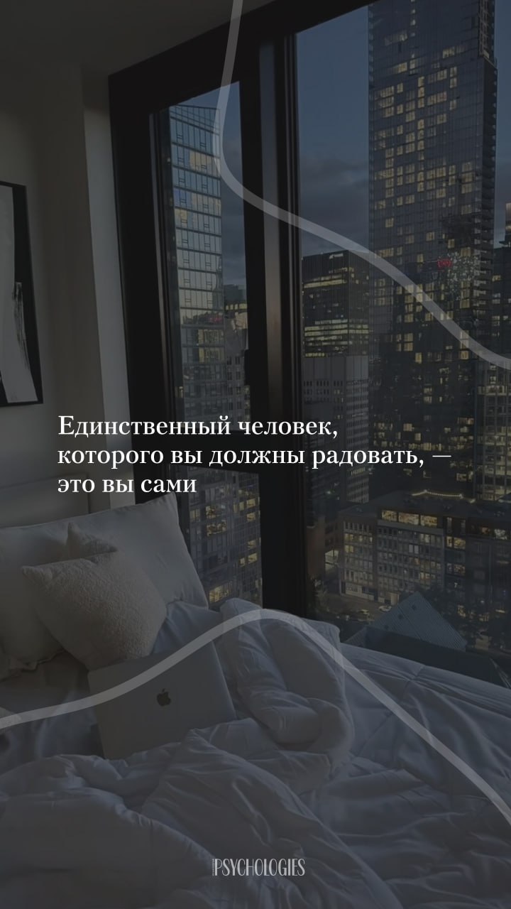Интерьер спальни у панорамного окна с видом на освещённый городской пейзаж ночью, мягкая постель и ноутбук на кровати создают атмосферу уюта