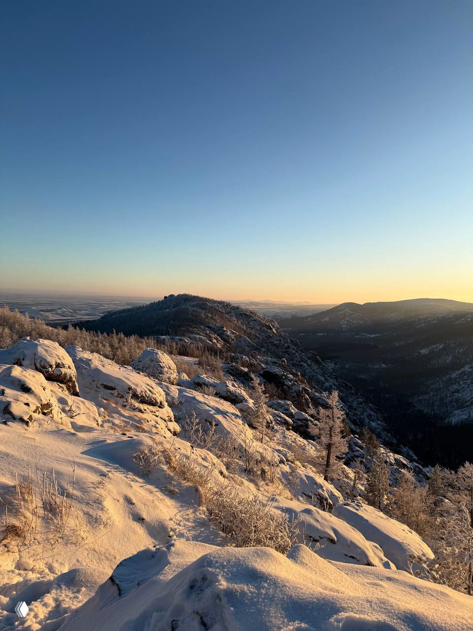 Панорамный вид на заснеженные скалы и леса с вершины — золотой свет солнца подчёркивает рельеф и морозные деревья.