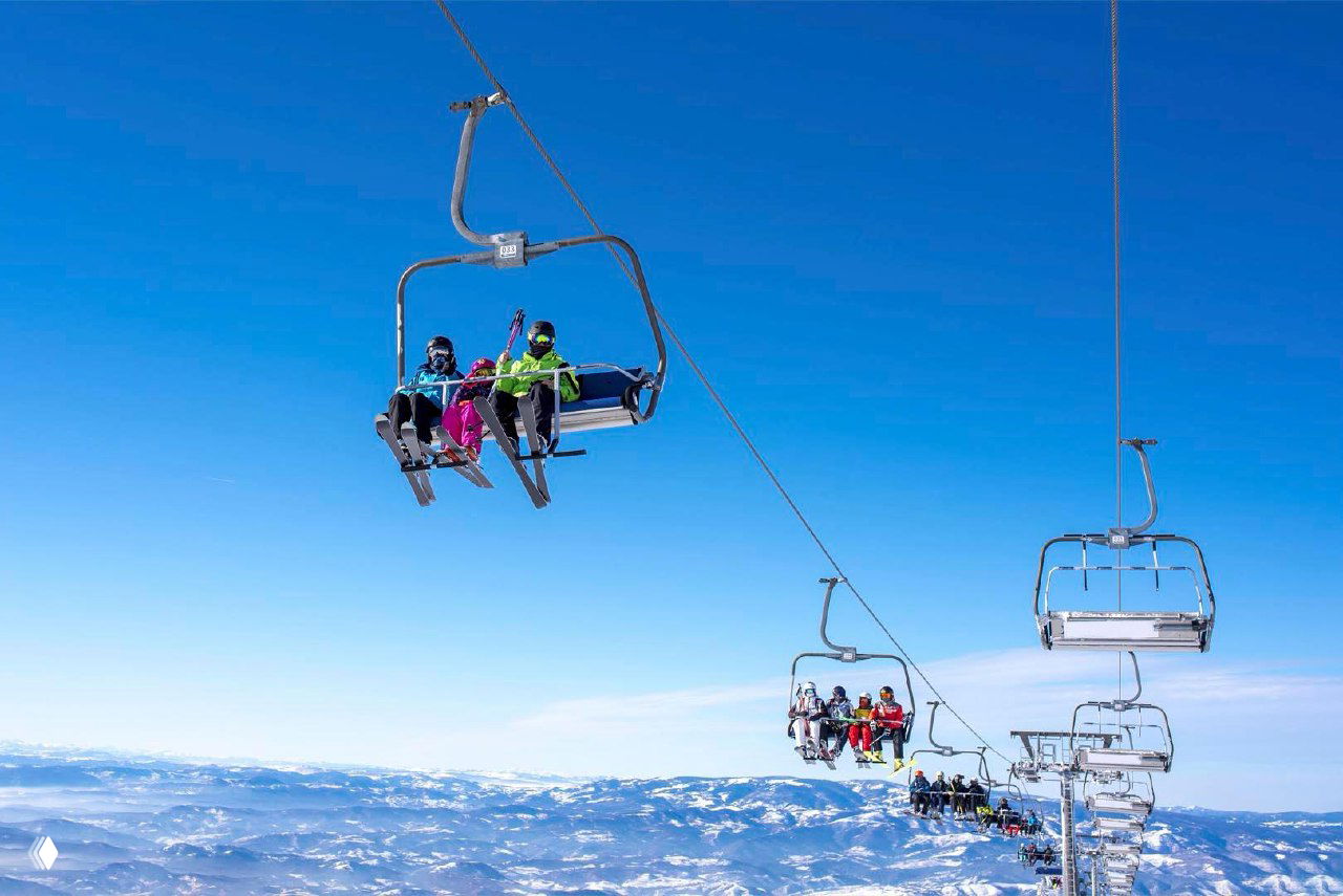 Группа лыжников на кресельном подъёмнике под чистым синим небом, кадр подчёркивает удобство подъёмников и масштабы зоны катания.