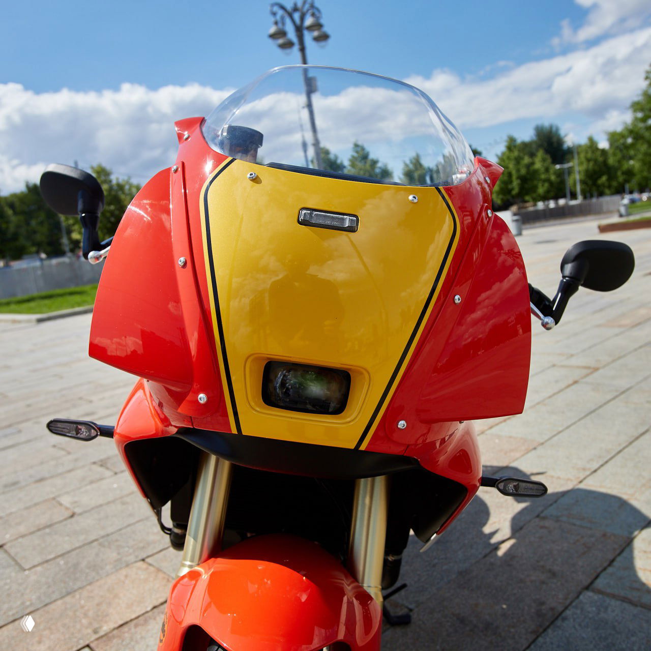 Крупный план передней части Yamaha XSR900 GP: ярко‑красно‑жёлтый почти гоночный обтекатель и маленькая прямоугольная фара под стеклом.