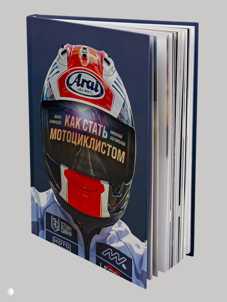 Твердый переплет книги «Как стать мотоциклистом» крупным планом — обложка с ярким шлемом, видны срезы страниц и плотный блок.