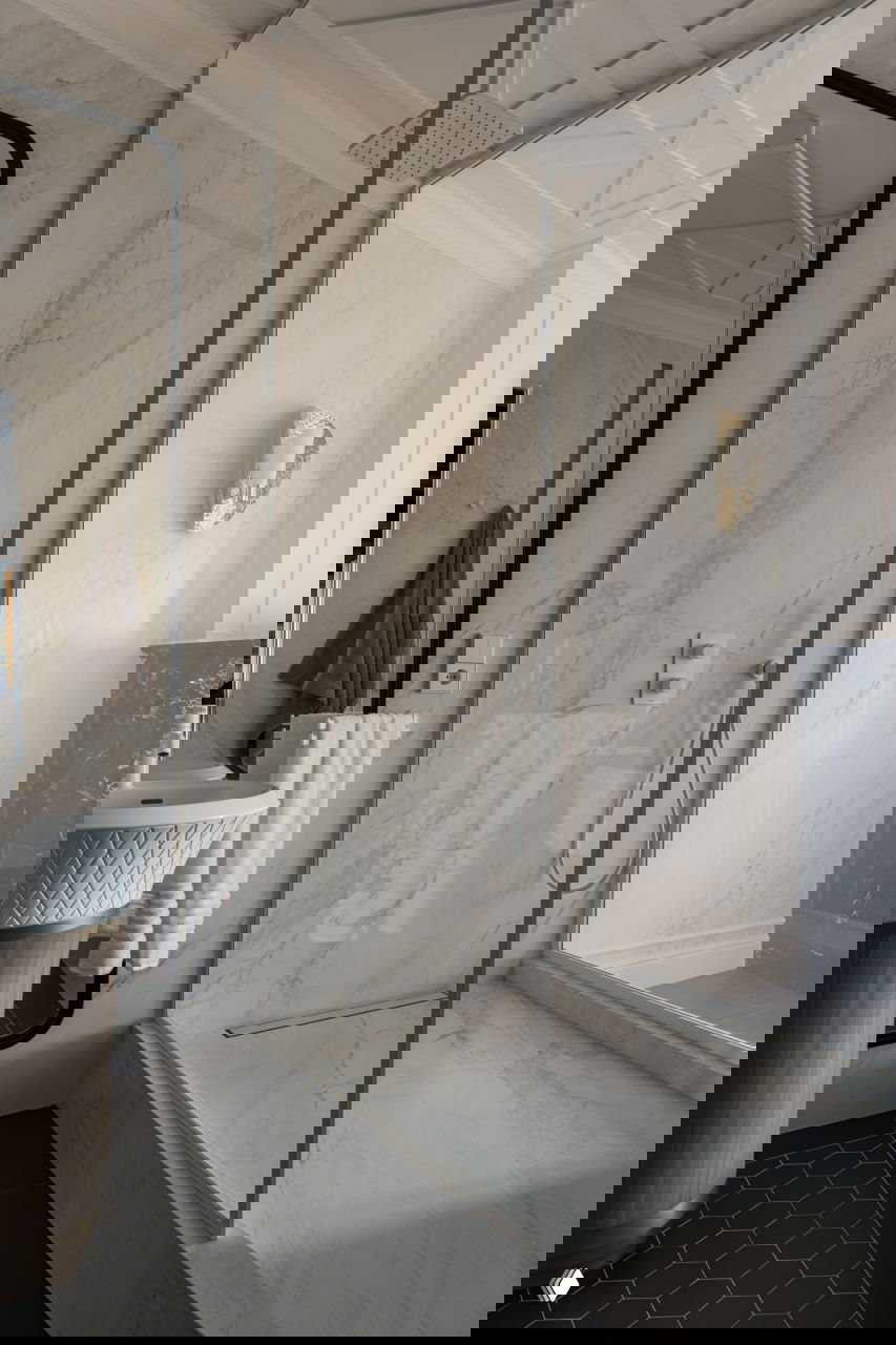 Крупный план прозрачной стеклянной перегородки в мраморной ванной с тропическим душем и зеркалом — акцент на чистых линиях и отделке.