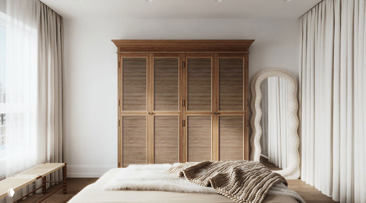 Фрагмент интерьера: массивный деревянный шкаф с жалюзийными фасадами напротив кровати, пол и текстиль в тёплых природных оттенках.