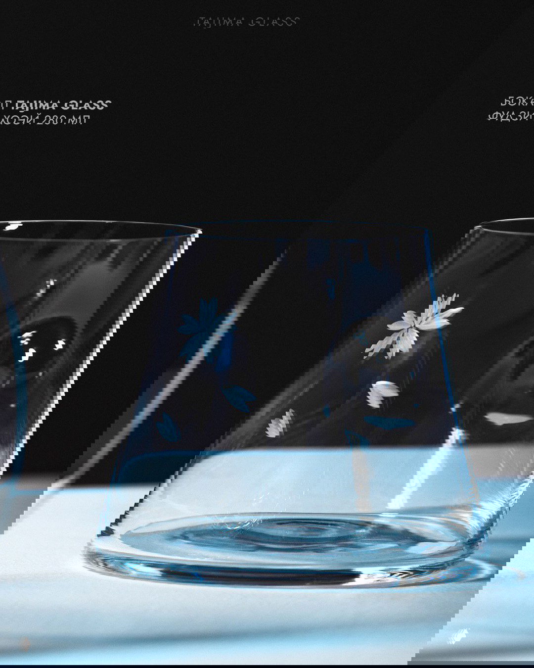 Прозрачный бокал Tajima Glass с тонкой гравировкой цветочных бутонов на тёмном фоне, демонстрирующий чистоту и мастерство шлифовки.