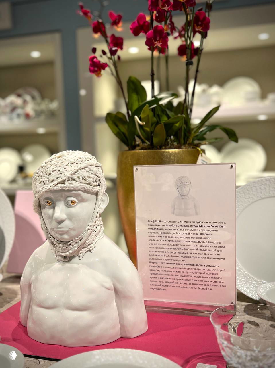 Белая брутальная скульптура бюста на витрине на фоне орхидеи и сервировки — сочетание искусства и декора в торговом пространстве.