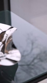 Крупный план полированного сервировочного предмета Georg Jensen на стеклянной поверхности с отражением и мягким боковым освещением.