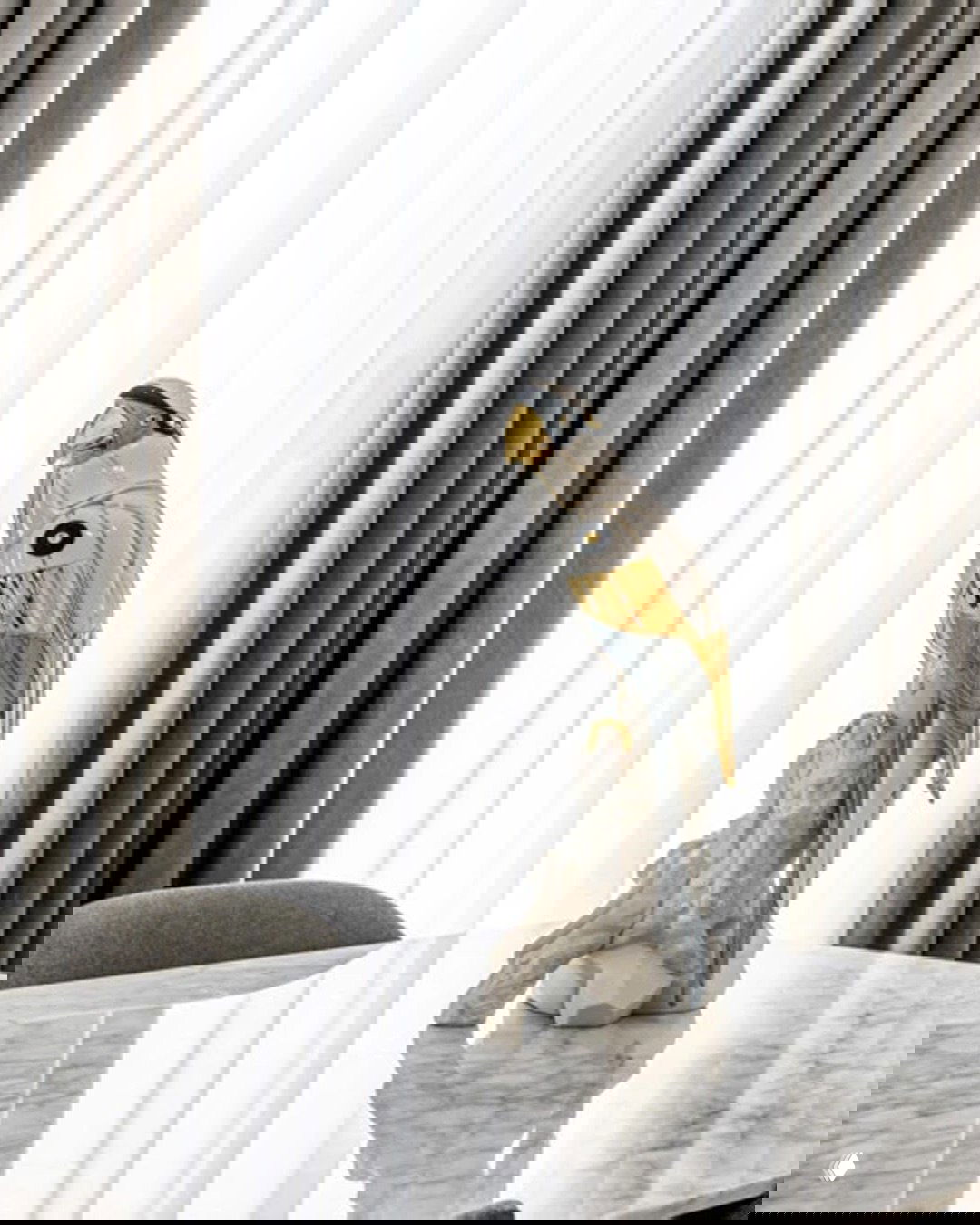 Фигурка «Попугай Ара‑киборг» Lladro на мраморном столе: глянец фарфора, золотые и металлические акценты в интерьере.