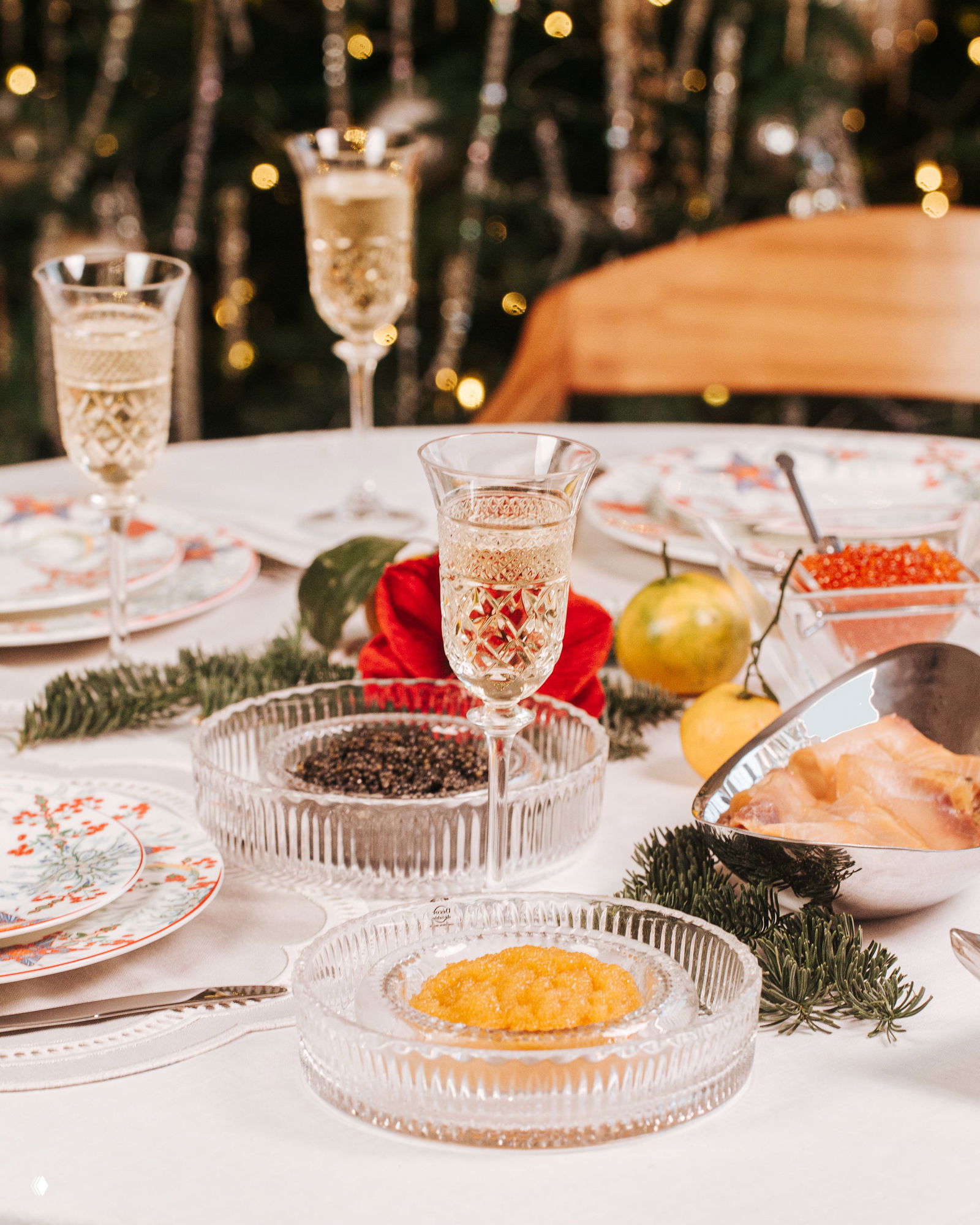 Детали стола: хрустальные блюда с икрой, тарелки с праздничным рисунком и елочные ветки — композиция для праздничной сервировки.