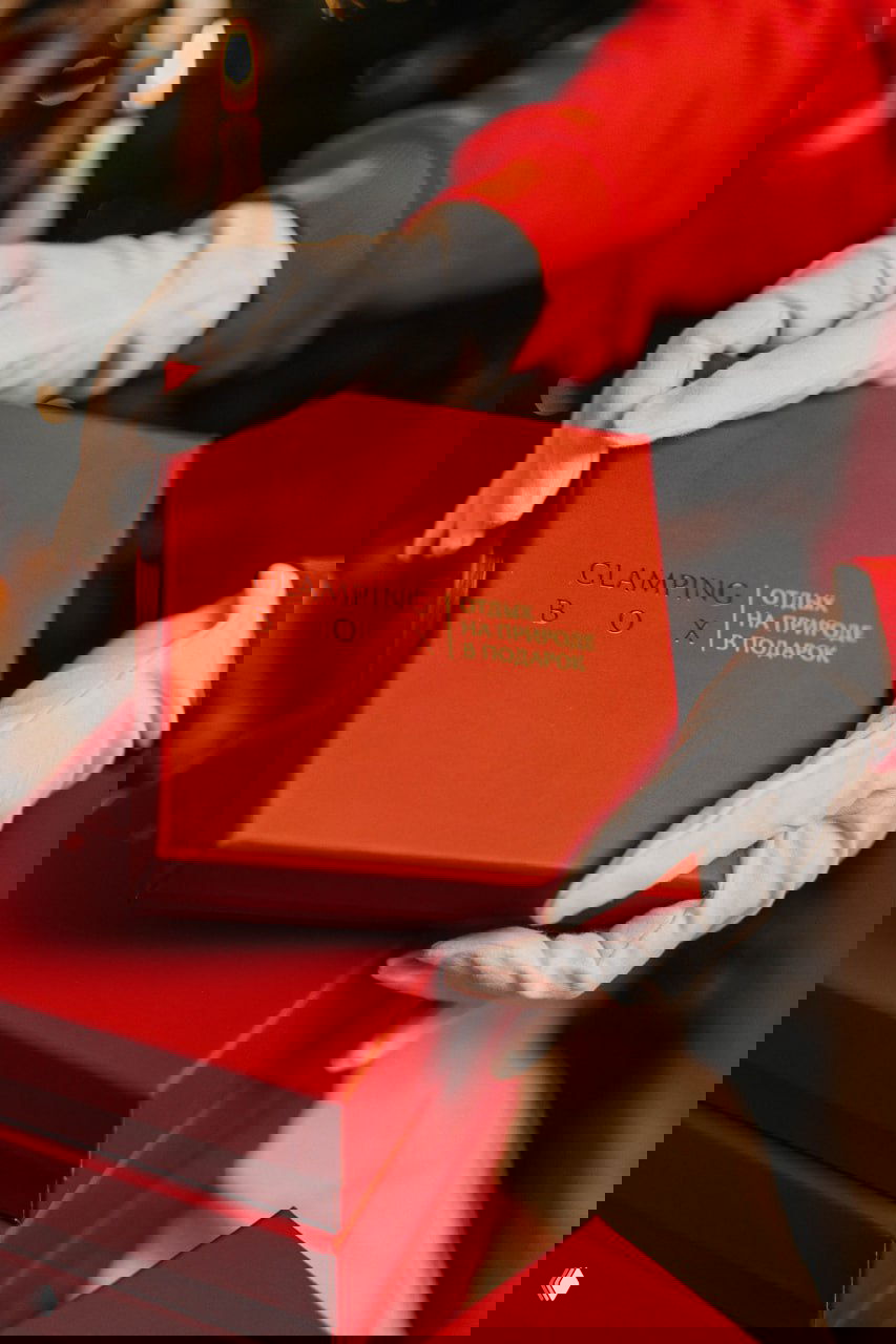 Руки в белых перчатках держат красную коробку Glamping Box с тиснённым логотипом — демонстрация премиальной упаковки подарка.