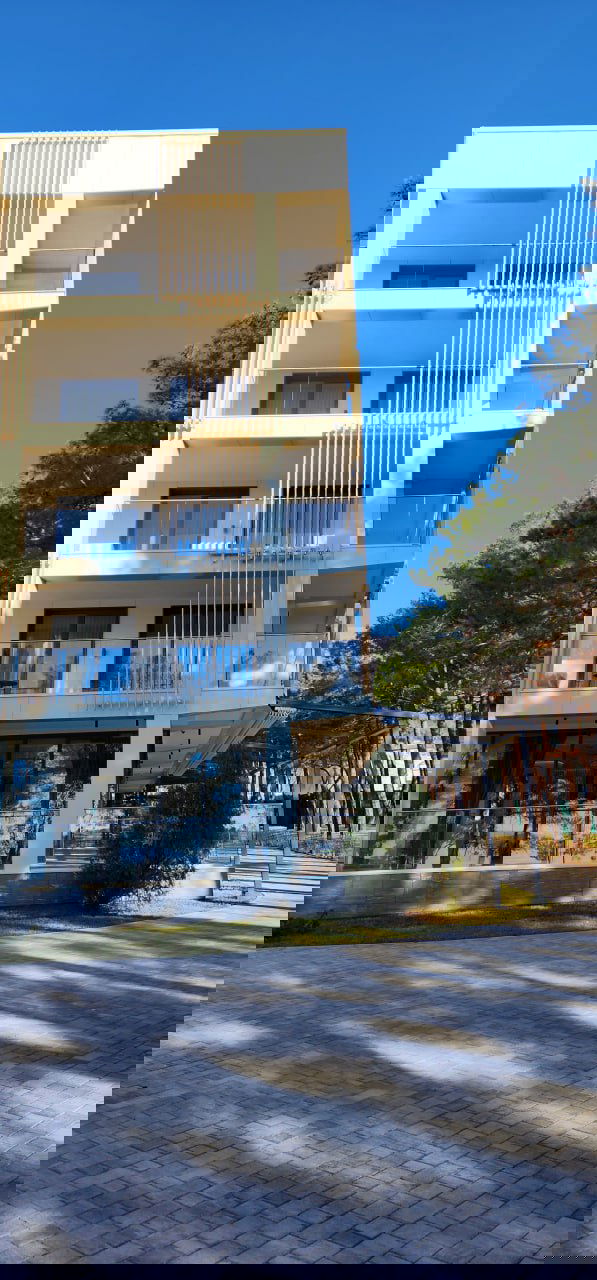 Фасад современного корпуса санатория с балконами, стеклянными перилами и элементами декора на фоне яркого голубого неба.