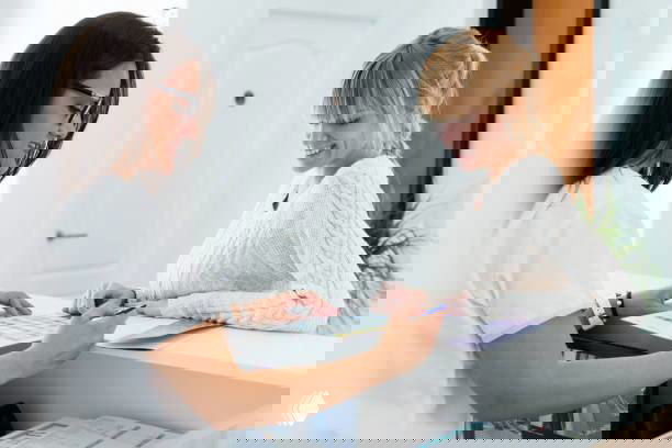 Администратор салона за стойкой ресепшн показывает клиентке варианты даты следующего визита — иллюстрация оперативной записи на следующий раз и коммуникации с клиентом.