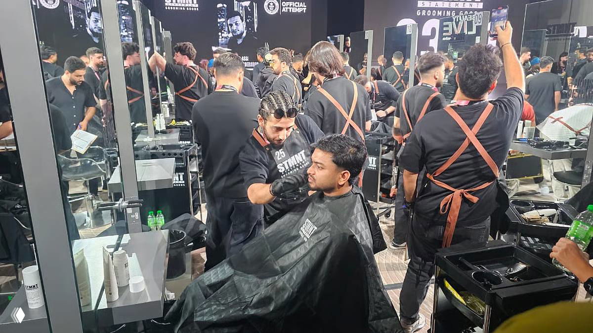 Фото с Beautyworld Middle East: барбер стрижет клиента в накидке у зеркала, вокруг коллеги в фартуках и рабочие станции.