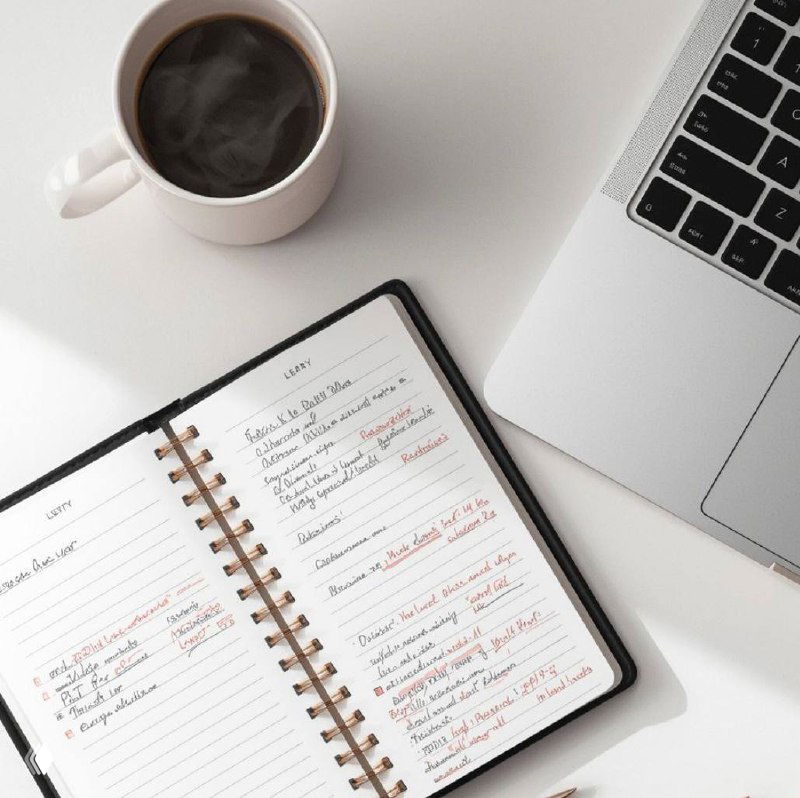 Открытый блокнот с записями, ручкой и клавиатурой на столе рядом с чашкой кофе — деловая сцена для ритуала управленца.