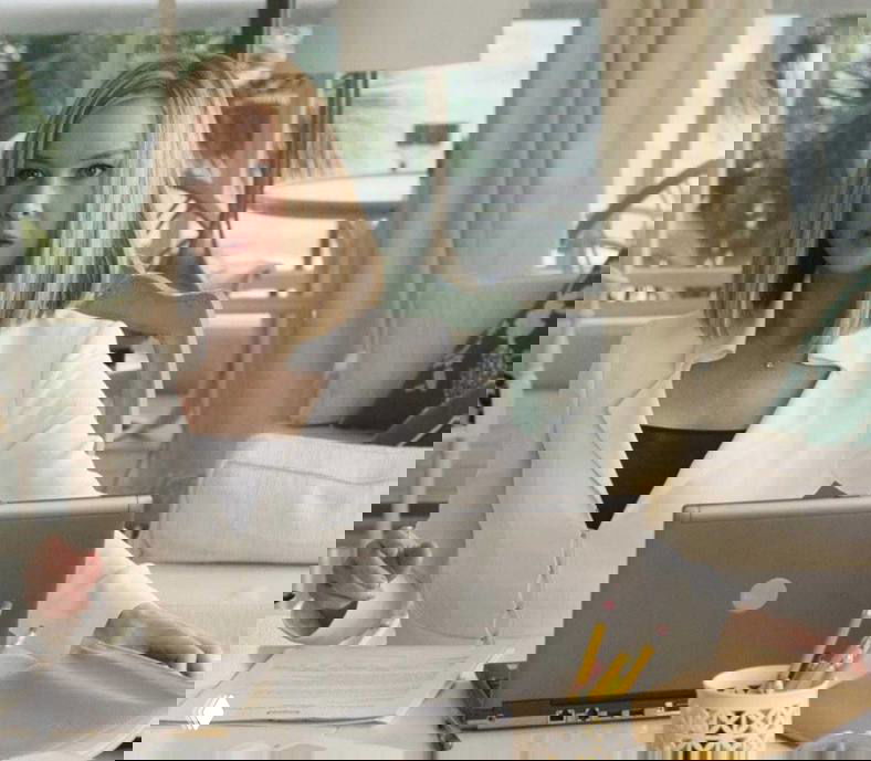 Женщина в светлом пиджаке сидит за письменным столом с ноутбуком и канцелярией; кадр создаёт деловую, спокойную атмосферу.