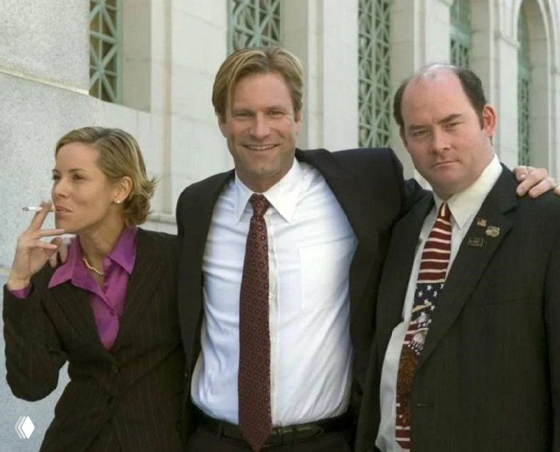 Трое людей в деловых костюмах улыбаются на улице у здания; кадр передаёт деловую, командную и дружелюбную атмосферу.