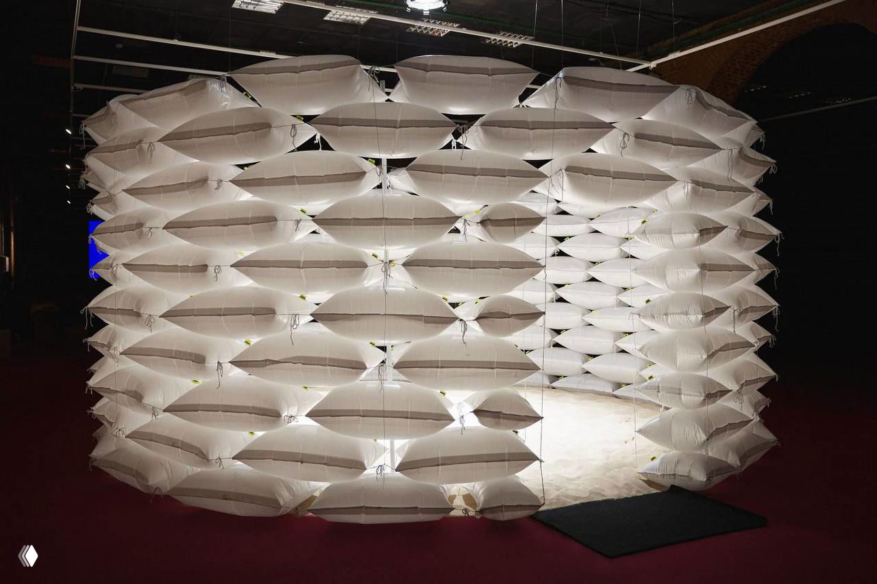 Инсталляция из белых надувных модулей и подсветки, образующая мягкое ограждение и создающая ощущение уединённой зоны для отдыха.