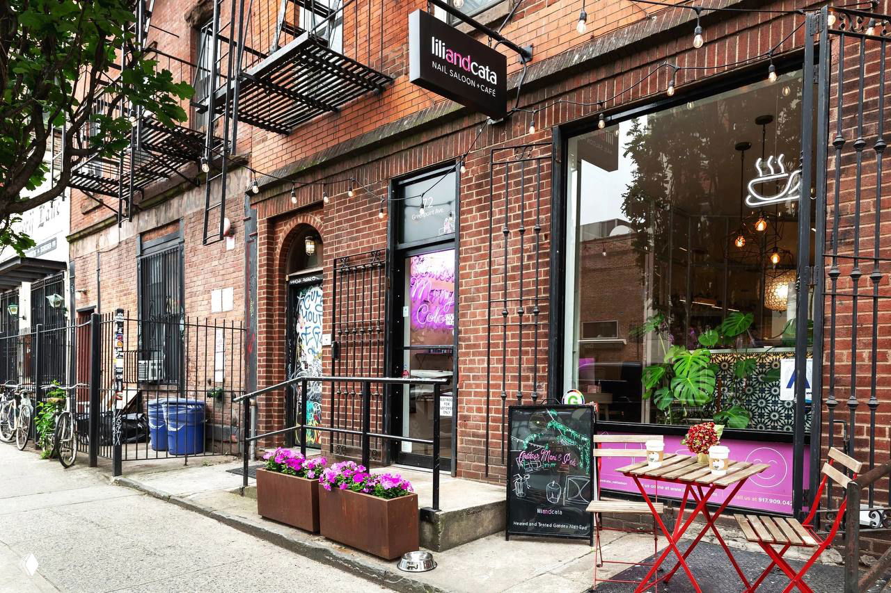 Фасад Lili and Cata Nail Saloon в Бруклине: кирпичная витрина с вывеской, уличный столик, цветочные ящики и элементы уличного кафе у входа.