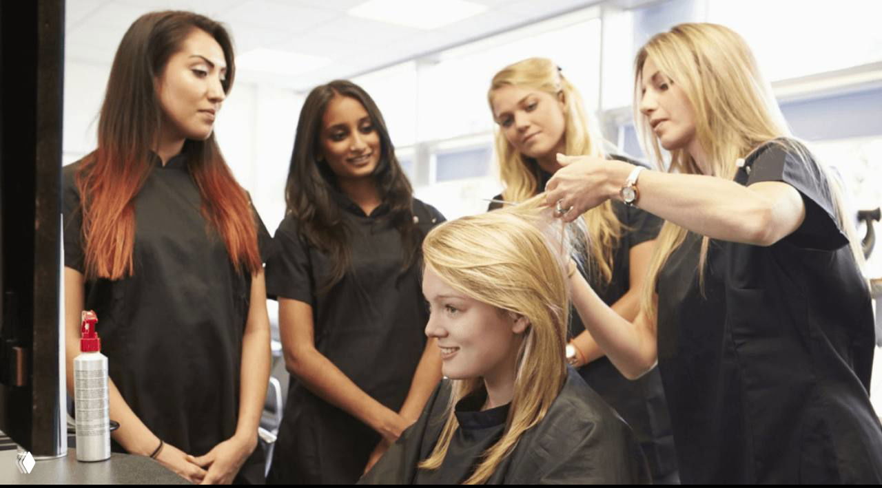 Мастера салона вокруг клиентки: старший специалист показывает технику, команда наблюдает во время обучения.