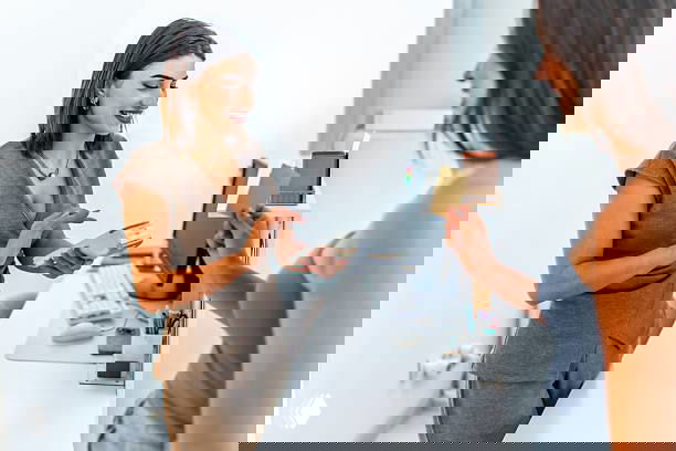 Две женщины на ресепшне: сотрудница принимает оплату и общается с клиенткой в офисной среде, иллюстрация взаимодействия и сервиса.